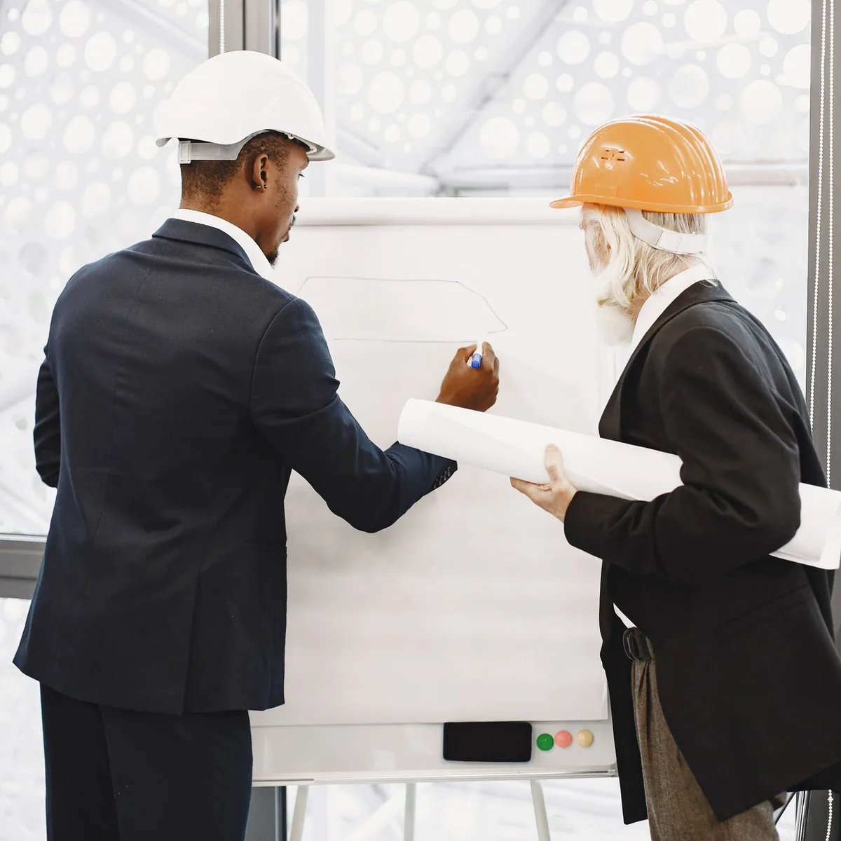 Two managers in hard hats discussing a plan at a whiteboard