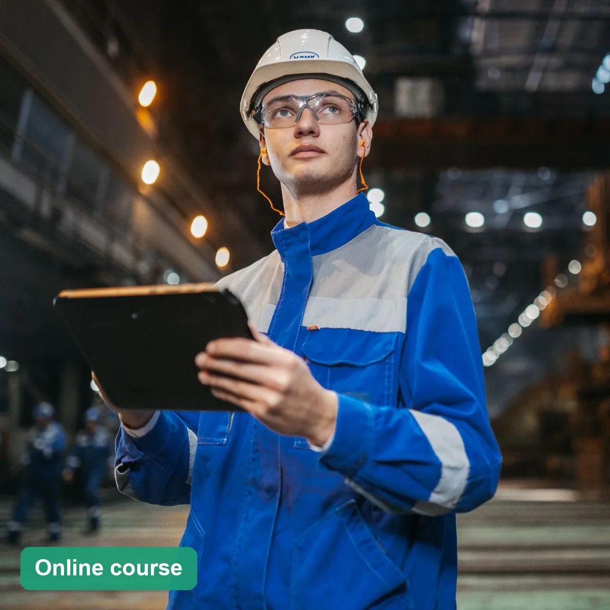 Worker in PPE assessing a factory work area with a tablet (online course)